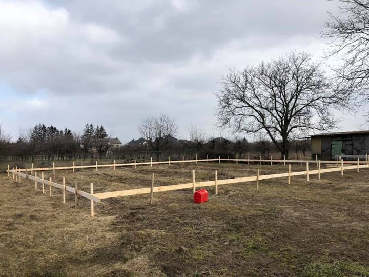 Wytyczenie fundamentów pod budowę domu, drewniane stemple i deski tworzące obrys na zewnątrz działki, czerwony kanister w rogu.