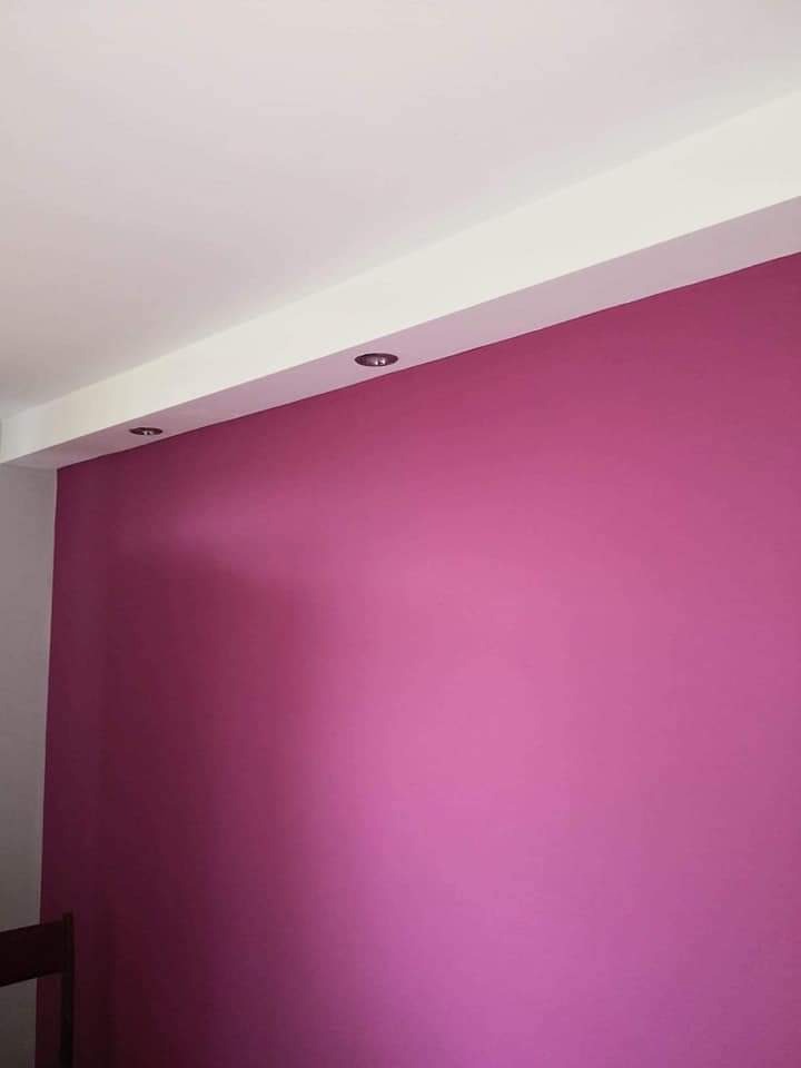Ściana pomalowana na intensywny różowy kolor z zamontowanymi punktowymi lampkami w suficie podwieszanym.