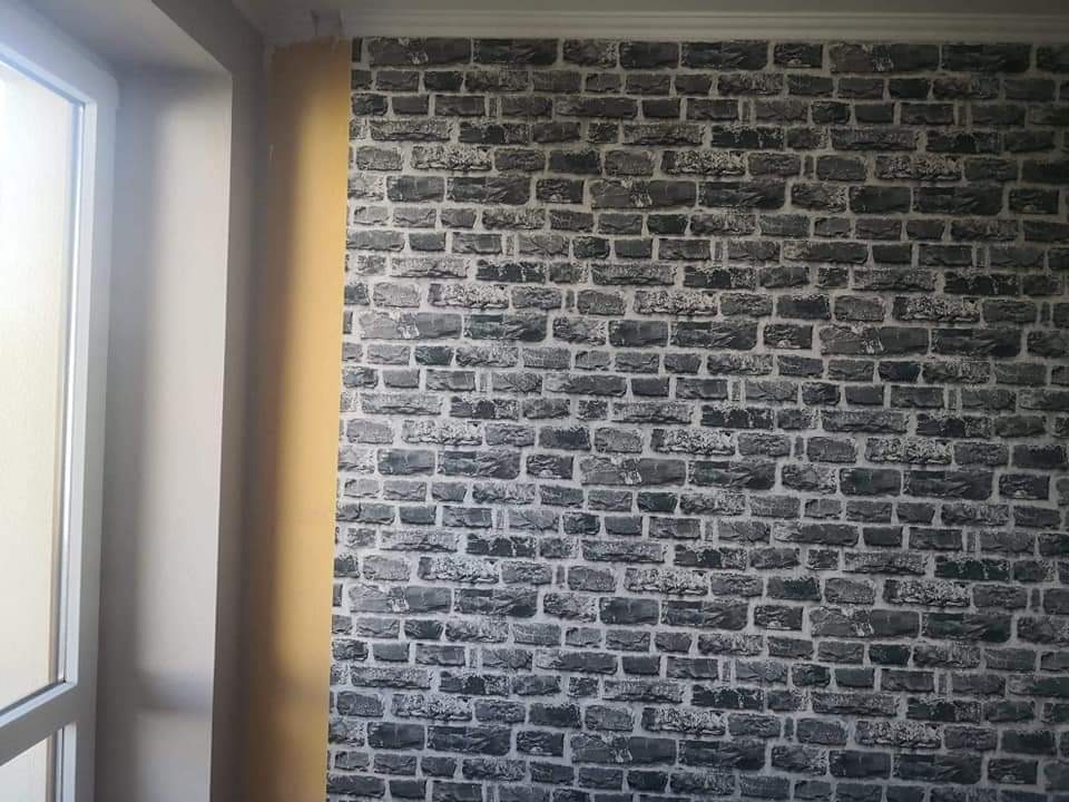 Ściana wykończona tapetą imitującą szarą cegłę, widok z boku okna, widoczna listwa przysufitowa.