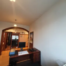 Jasne biuro z biurkiem, komputerem i drukarką; widoczna gładka, pomalowana na biało ściana.