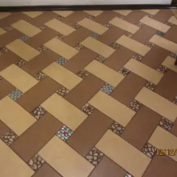 Ułożona w jodełkę podłoga z płytek w odcieniach brązu i beżu, z dekoracyjnymi wstawkami imitującymi kamień i mozaikę, widoczna data wykonania na zdjęciu.