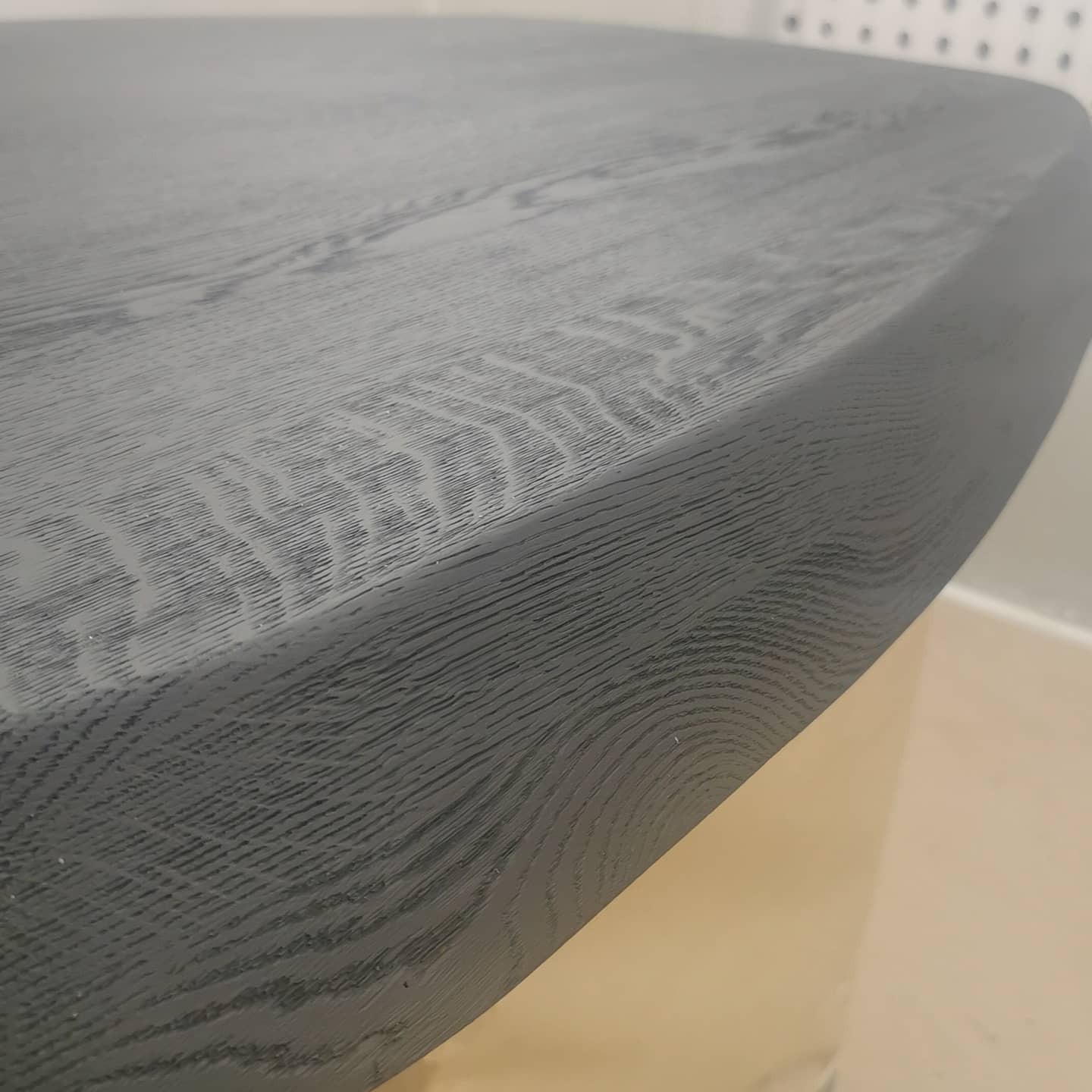 Fragment okrągłego blatu z ciemnego drewna z widocznym usłojeniem, wykończonego na wysoki połysk.