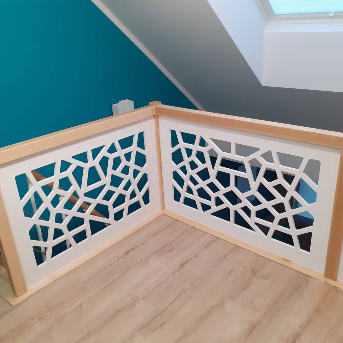 Ażurowa barierka z geometrycznym wzorem, drewniane wykończenie, turkusowa ściana w tle, poddasze z oknem dachowym.
