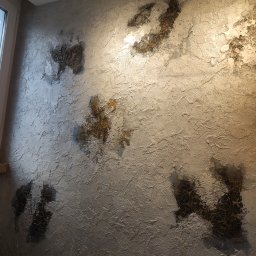 Kalmia Enterprise Sp zoo - Dekoracyjna ściana z fakturą i ciemnymi, okrągłymi wzorami przypominającymi mandale, oświetlona od góry, z widocznym gniazdkiem elektrycznym w dolnej części.