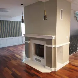 Nowoczesny salon z kominkiem obłożonym marmurem, drewnianą podłogą parkietową i wiszącymi lampami z metalowymi detalami.