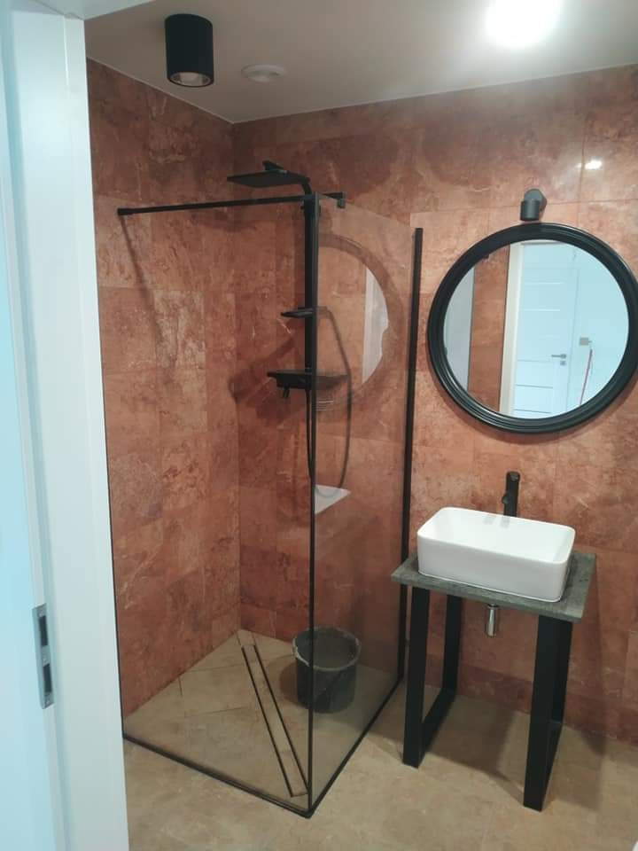 Nowoczesna kabina prysznicowa z czarnymi profilami i deszczownicą, umywalka nablatowa na metalowym stelażu oraz okrągłe lustro w czarnej ramie w łazience w Warszawie wykończonej płytkami...