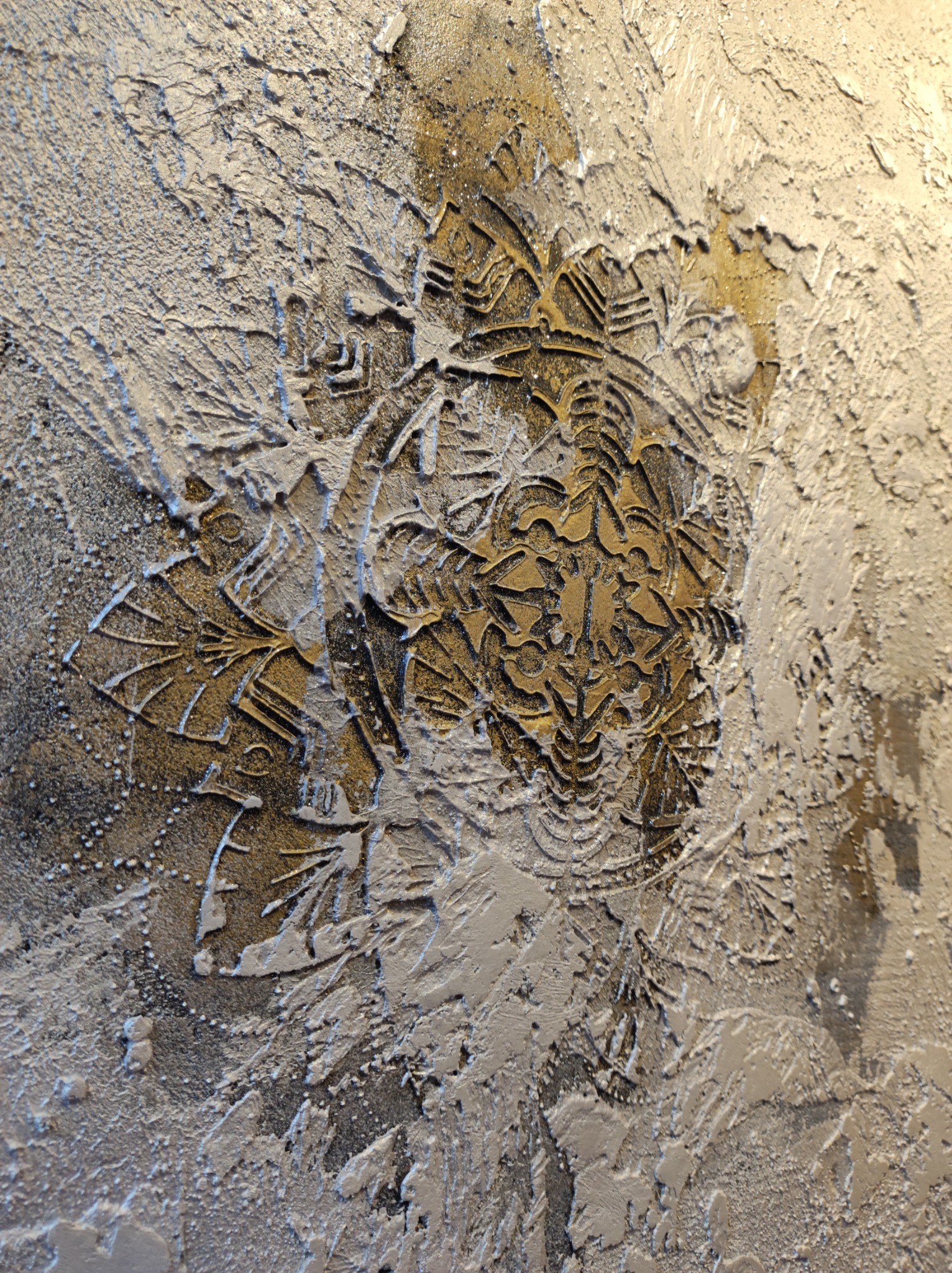 Dekoracyjna struktura ściany z wyraźnym, wypukłym motywem roślinnym w odcieniach złota i srebra, wykonana techniką reliefu.