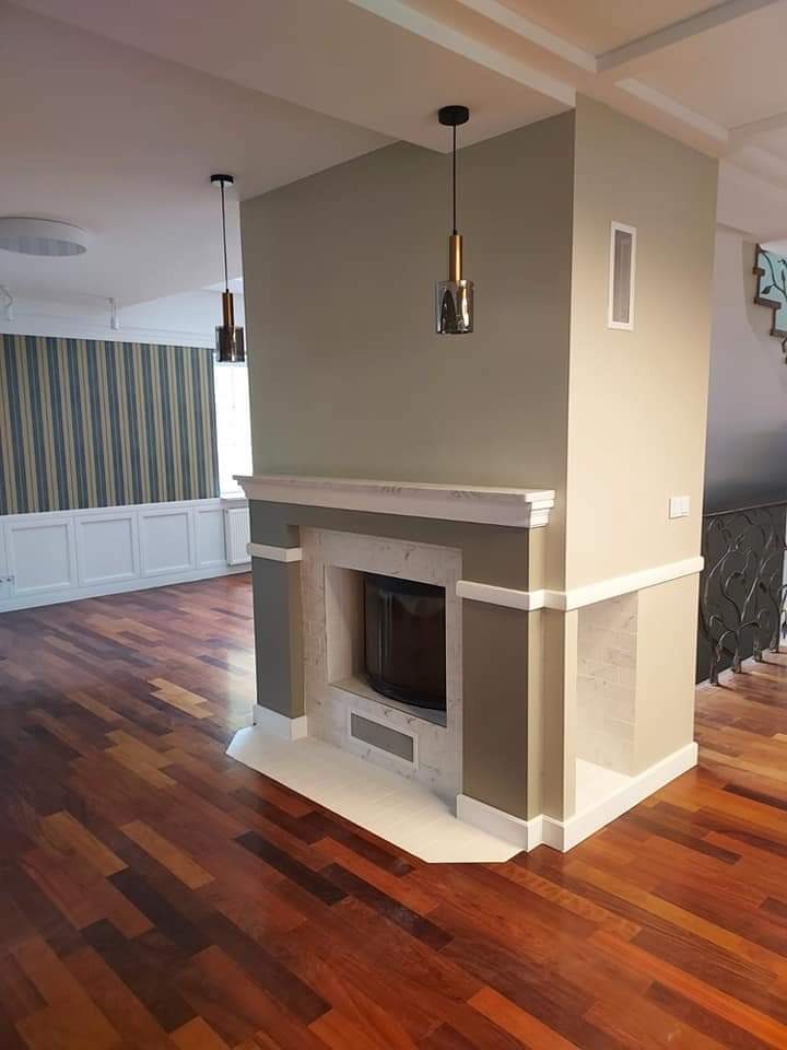 Nowoczesny salon z kominkiem obłożonym marmurem, drewnianą podłogą parkietową i wiszącymi lampami z metalowymi detalami.