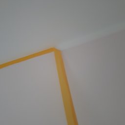 Groch-Bud - Żółta taśma malarska zabezpieczająca narożnik ściany i sufit przed malowaniem, widok z dołu pod kątem.