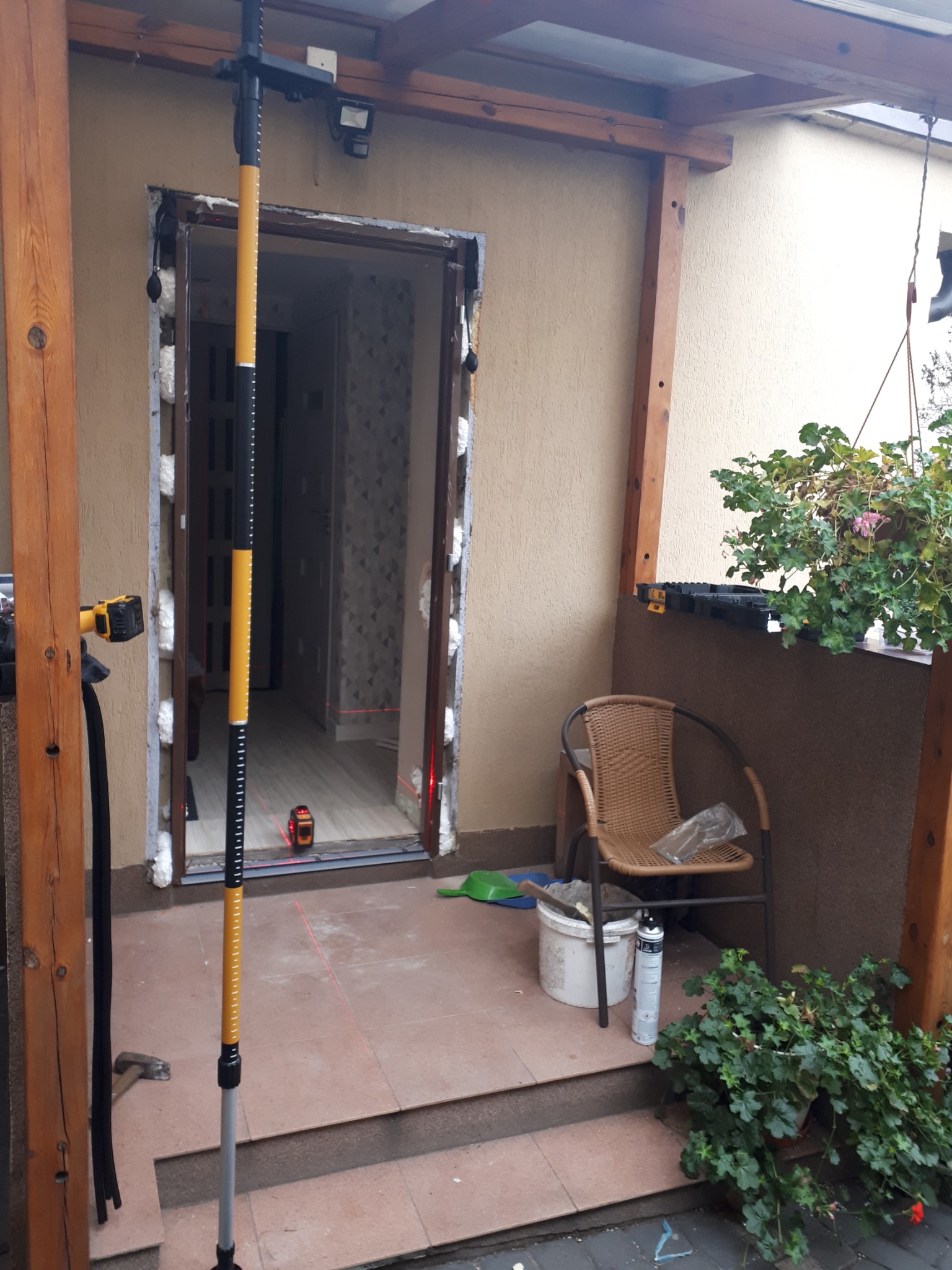 Przygotowanie do montażu drzwi zewnętrznych: ościeżnica uszczelniona pianką montażową, poziomica laserowa wyznacza pion, widoczne narzędzia i materiały budowlane w otoczeniu.