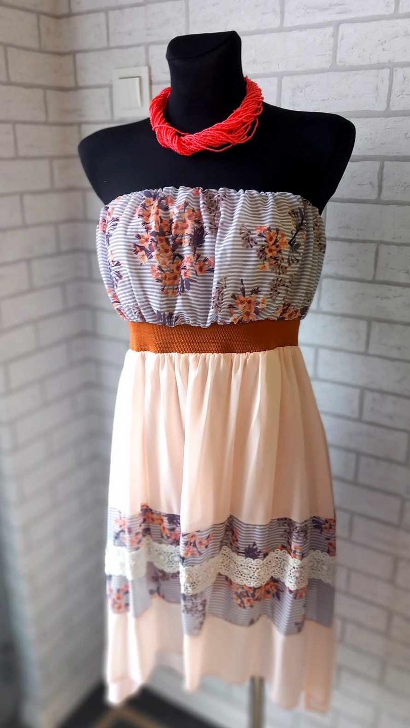 Letnia sukienka bez ramiączek z motywem kwiatowym i koronkowym wykończeniem na manekinie, uzupełniona o jaskrawoczerwony naszyjnik z koralików.