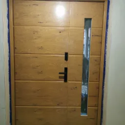 Nowoczesne drzwi wejściowe z przeszkleniem pionowym, wykończone okleiną imitującą drewno, widoczne ślady prac montażowych na ścianie i futrynie.