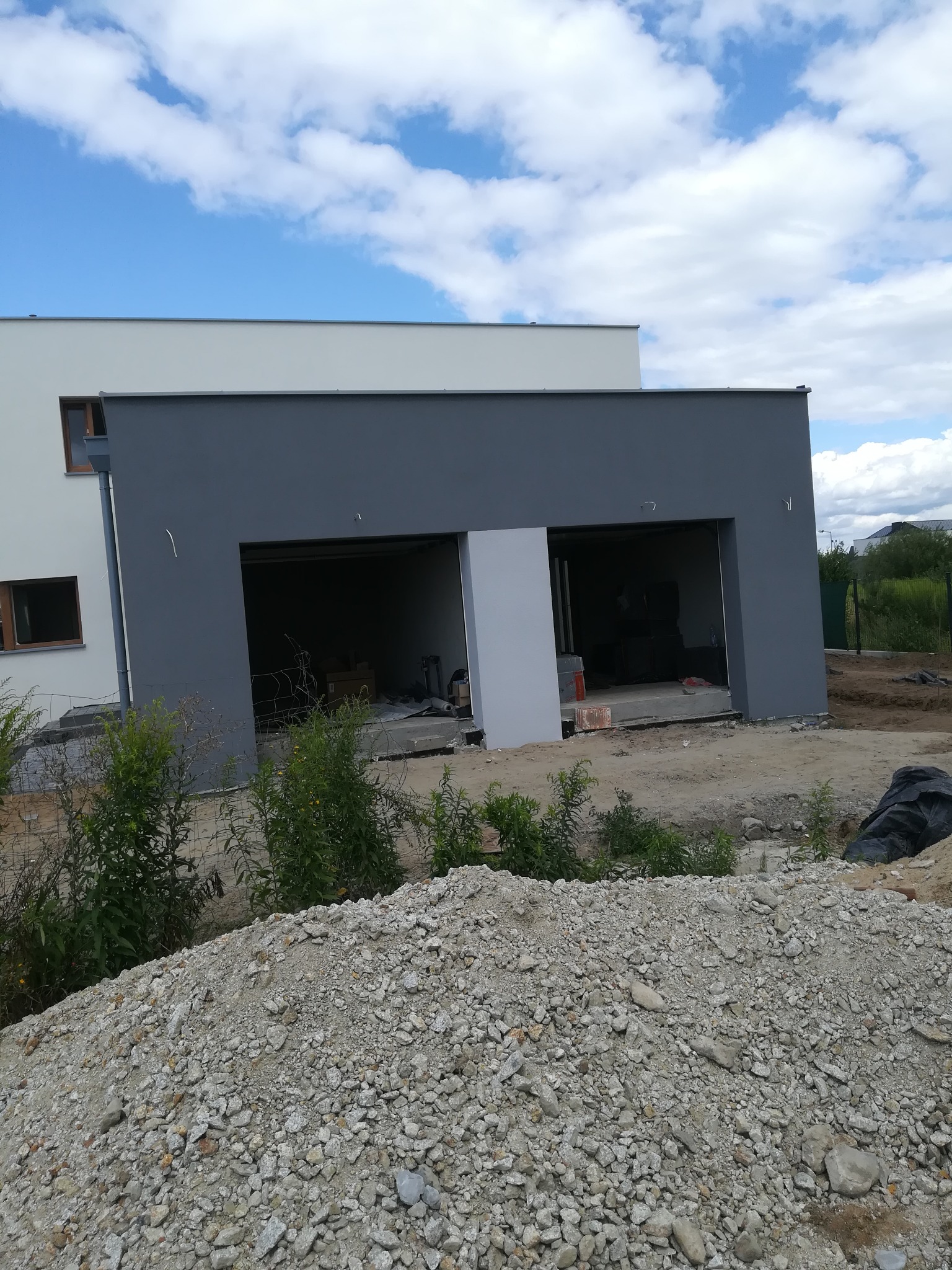 Nowoczesny dom z dwoma garażami w Margoninie, w trakcie budowy, widoczny stos gruzu przed budynkiem.