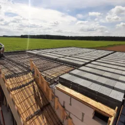 Prace nad stropem Teriva: robotnik siedzi na siatce zbrojeniowej, w tle widok na zielone pole i las.