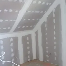 Pokój na poddaszu z ukończonymi płytami kartonowo-gipsowymi, widoczne szpachlowane łączenia i kable elektryczne wystające ze ściany.