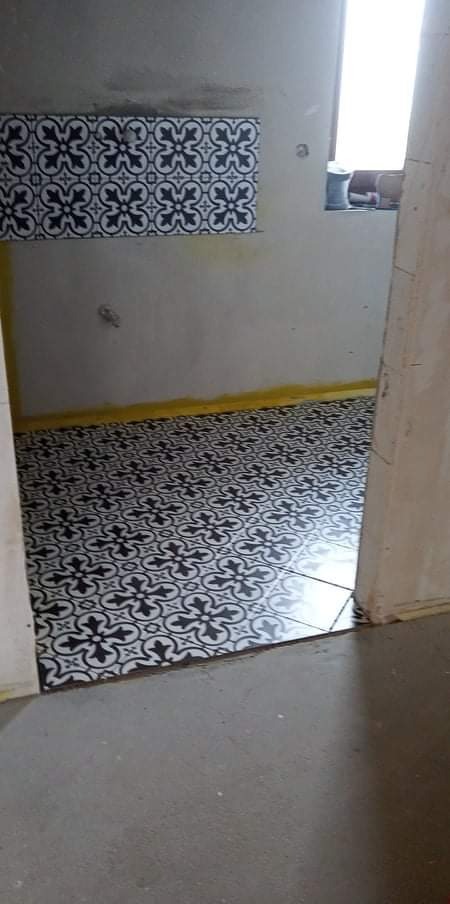 Ułożone czarno-białe płytki podłogowe z wzorem w pomieszczeniu w trakcie remontu, widoczne fragmenty surowych ścian i żółtej taśmy zabezpieczającej.