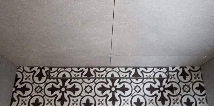 Fragment łazienki z szarymi płytkami na ścianach i suficie oraz dekoracyjnym pasem z czarno-białych płytek o wzorze geometrycznym.