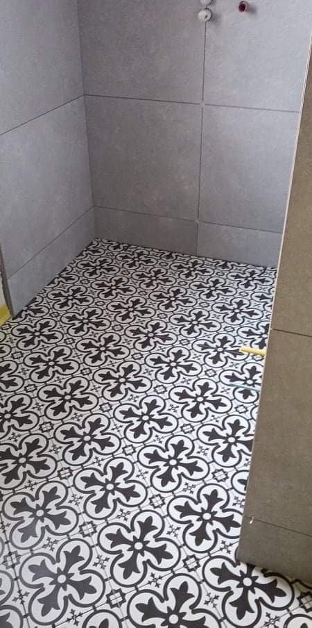 Ułożona podłoga z płytek ceramicznych w czarno-biały wzór kwiatowy w rogu łazienki z szarymi płytkami ściennymi.