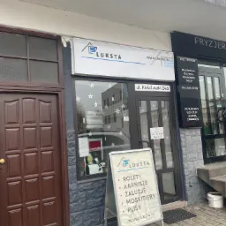 Fasada budynku firmy Luksta z szyldem i tablicą reklamową oferującą rolety, żaluzje, moskitiery i plisy, ul. Kościuszki 24a.