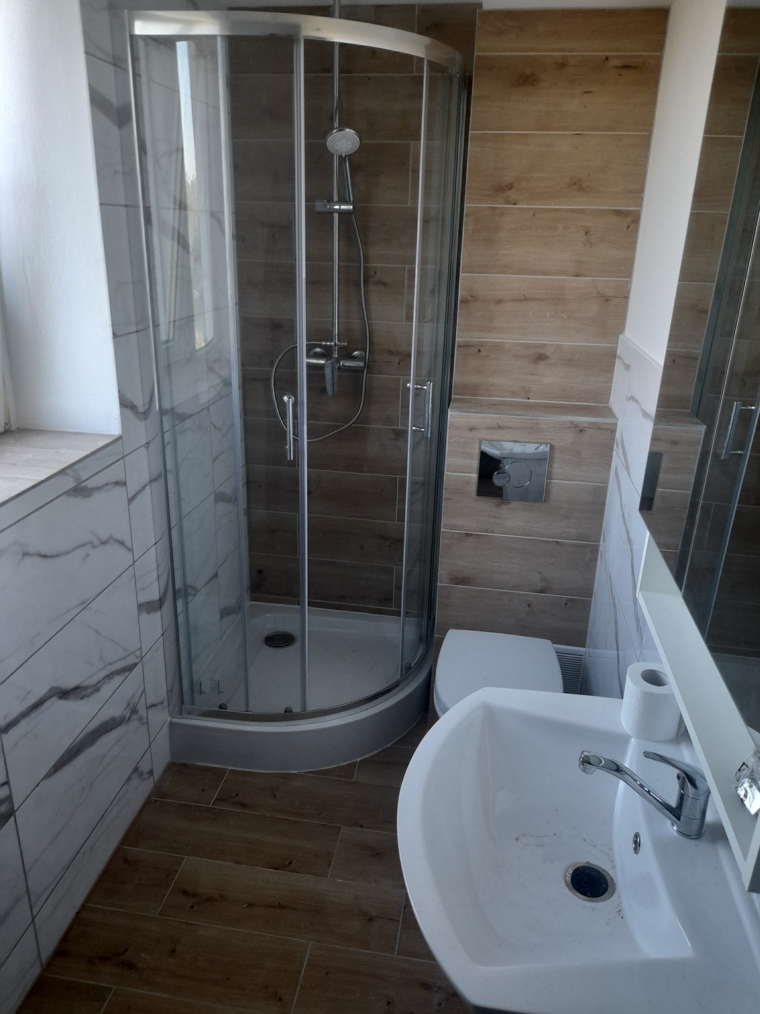 Wykończona łazienka w Sławnie z kabiną prysznicową z zaokrąglonymi drzwiami, umywalką i toaletą w neutralnej kolorystyce.