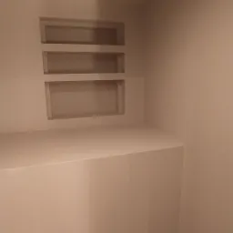 Wnęki ścienne z płyty karton gips, pomalowane na jasny kolor, z półką w dolnej części w rogu pokoju.