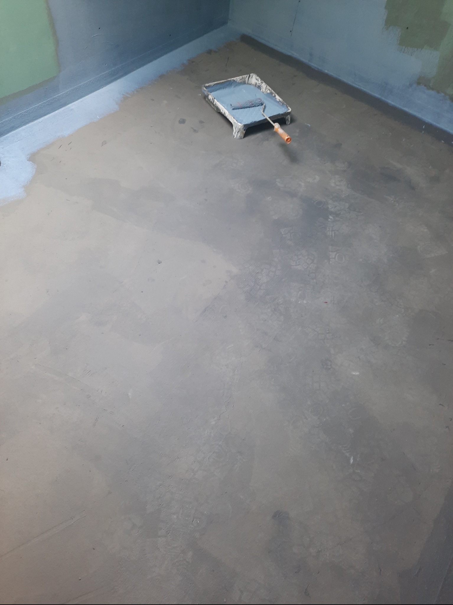 Świeżo pomalowana podłoga w szarym odcieniu, widoczna kuweta z wałkiem malarskim, ślady malowania na ścianach.