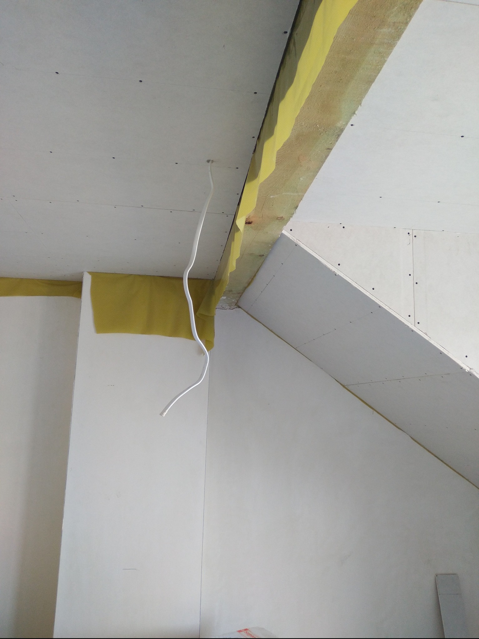Skośny sufit i ściana z płyt kartonowo-gipsowych, widoczne łączenia płyt i wystający kabel elektryczny.