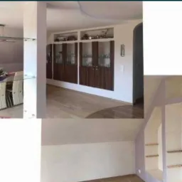 Wnętrze domu po remoncie: widok na jadalnię ze szklanym stołem, zabudowę meblową z przeszklonymi witrynami i wnęki w ścianie na poddaszu, świeżo pomalowane na jasny kolor.