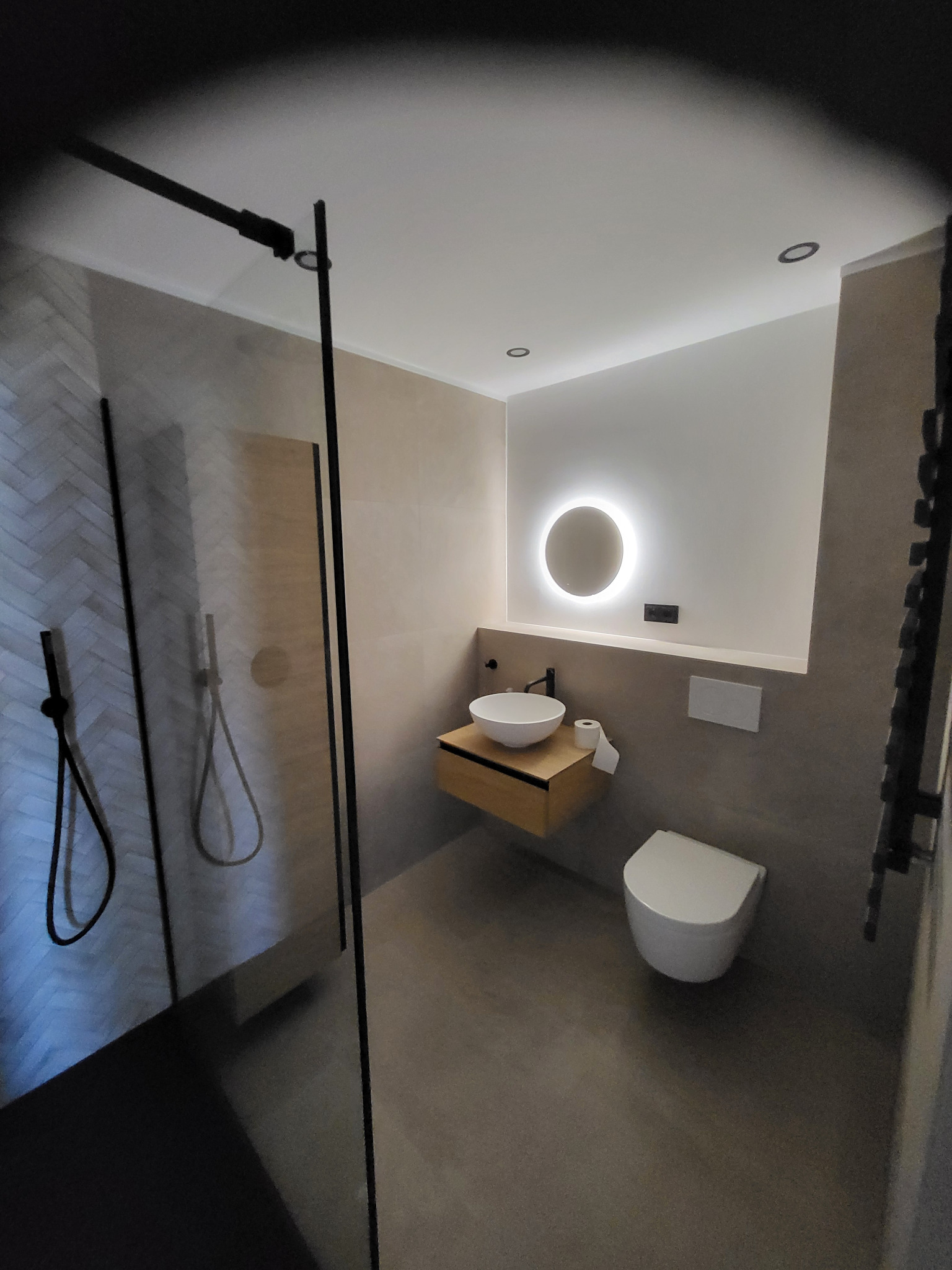 Nowoczesna łazienka z kabiną prysznicową typu walk-in, umywalką nablatową i podświetlanym lustrem. Minimalistyczny design, neutralna kolorystyka, płytki imitujące drewno.