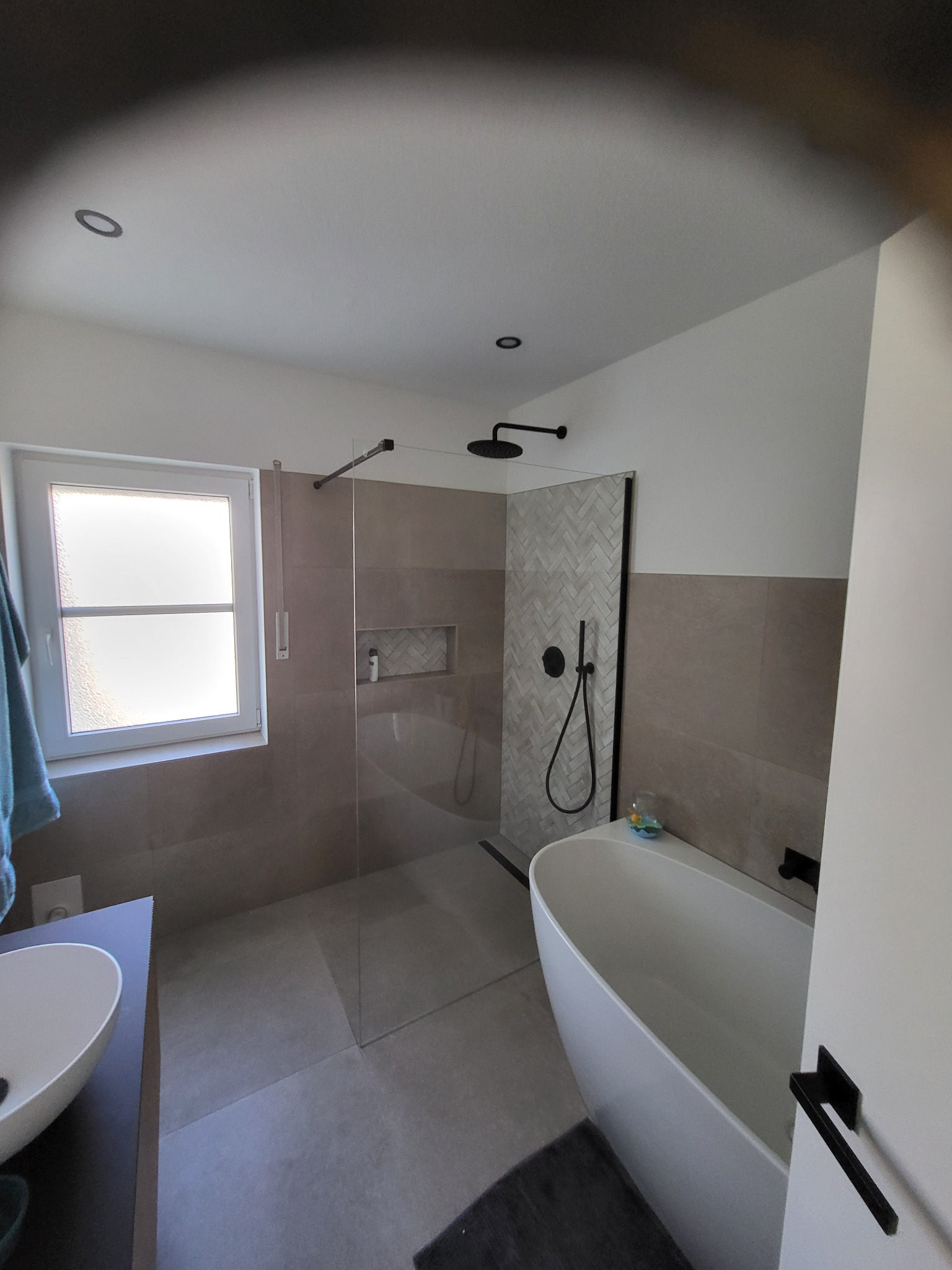 Nowoczesna łazienka z kabiną prysznicową typu walk-in, wolnostojącą wanną i umywalką nablatową. Uwagę zwraca ściana wykończona płytkami w jodełkę.