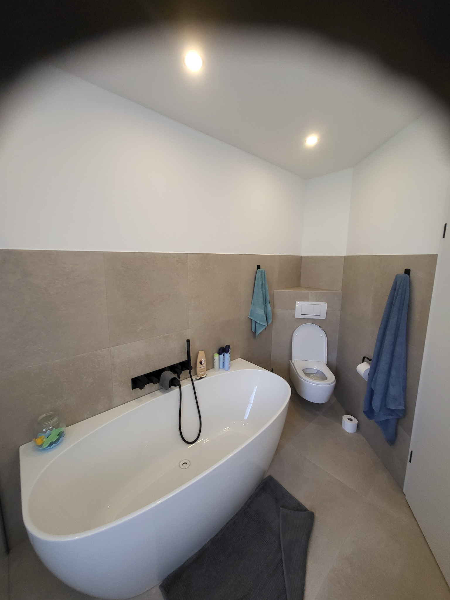 Nowoczesna łazienka z wolnostojącą wanną, beżowymi płytkami i minimalistyczną armaturą. Akcent kolorystyczny stanowią turkusowe ręczniki i dekoracje.