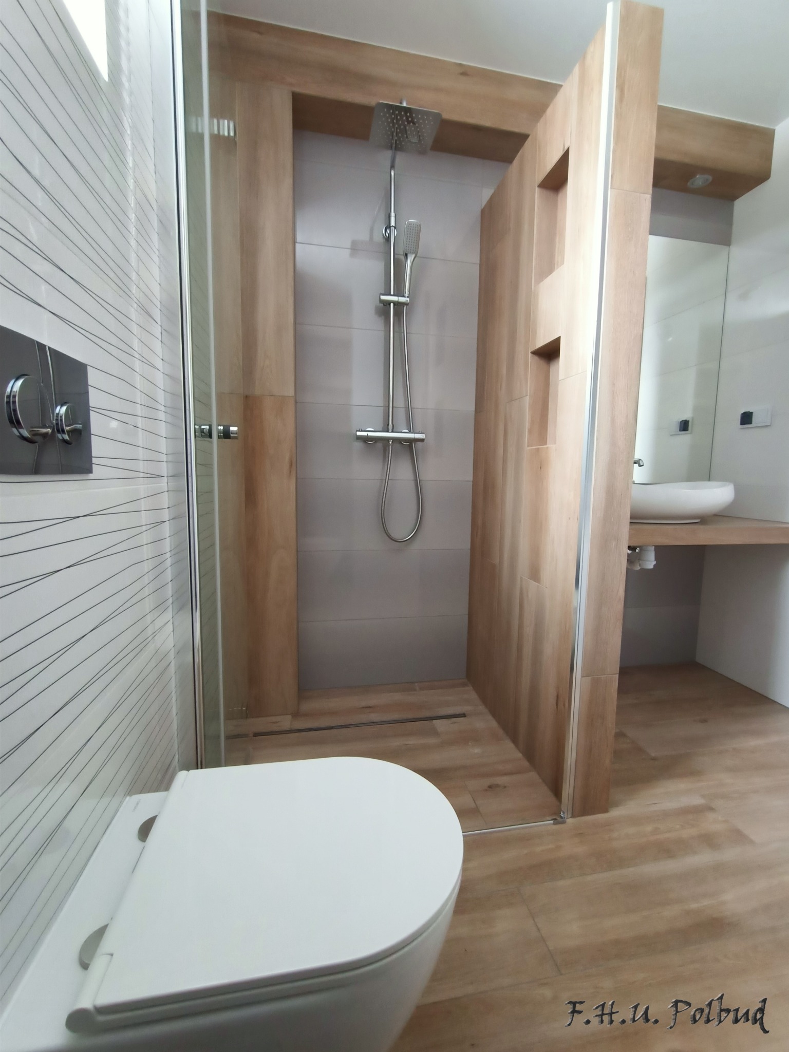 Nowoczesna łazienka z kabiną prysznicową typu walk-in, umywalką nablatową i toaletą podwieszaną, wykończona płytkami imitującymi drewno i białymi płytkami z delikatnym wzorem poziomych linii.