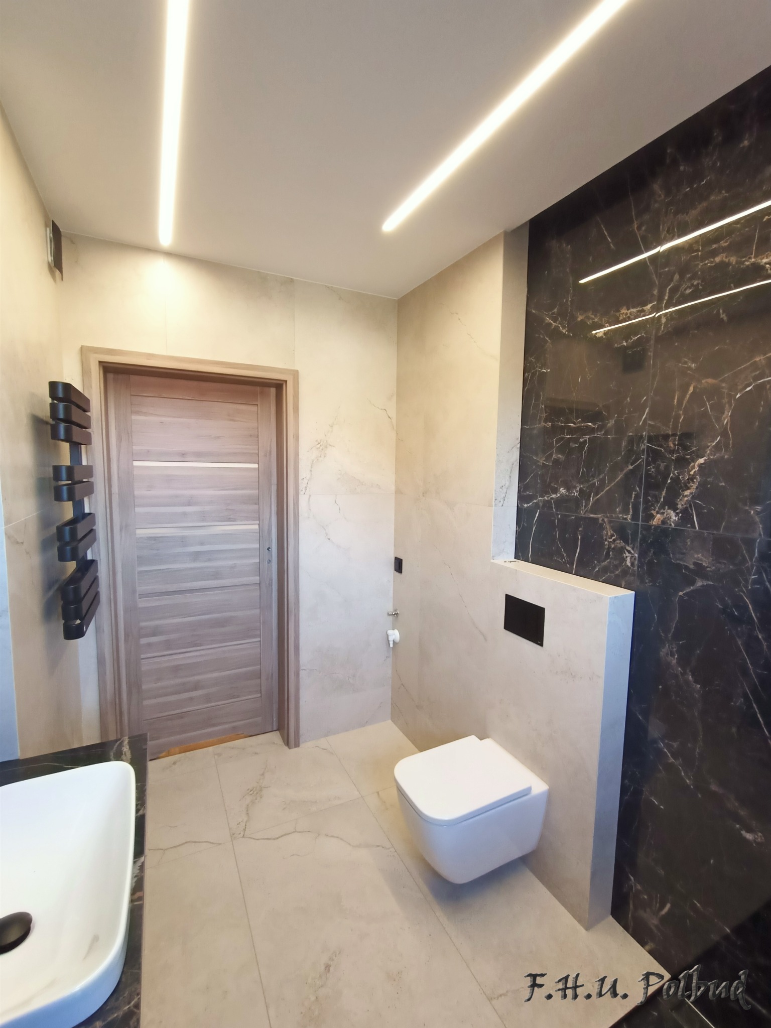 Nowoczesna łazienka z beżowymi płytkami imitującymi marmur, czarną ścianą z marmuru, podwieszaną miską WC i oświetleniem LED na suficie.