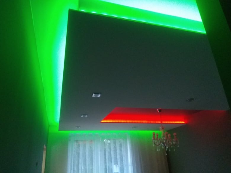 Sufit podwieszany z oświetleniem LED w kolorach zielonym i czerwonym, wykonany w Zabrzu, z widocznym żyrandolem i oknem z białymi firankami.