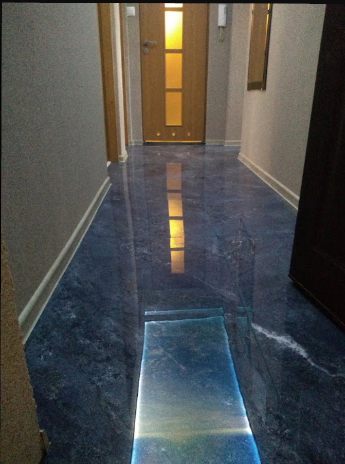 Błyszcząca, ciemnoniebieska posadzka imitująca marmur w korytarzu, z odbiciem światła z drzwi i fragmentem progu.