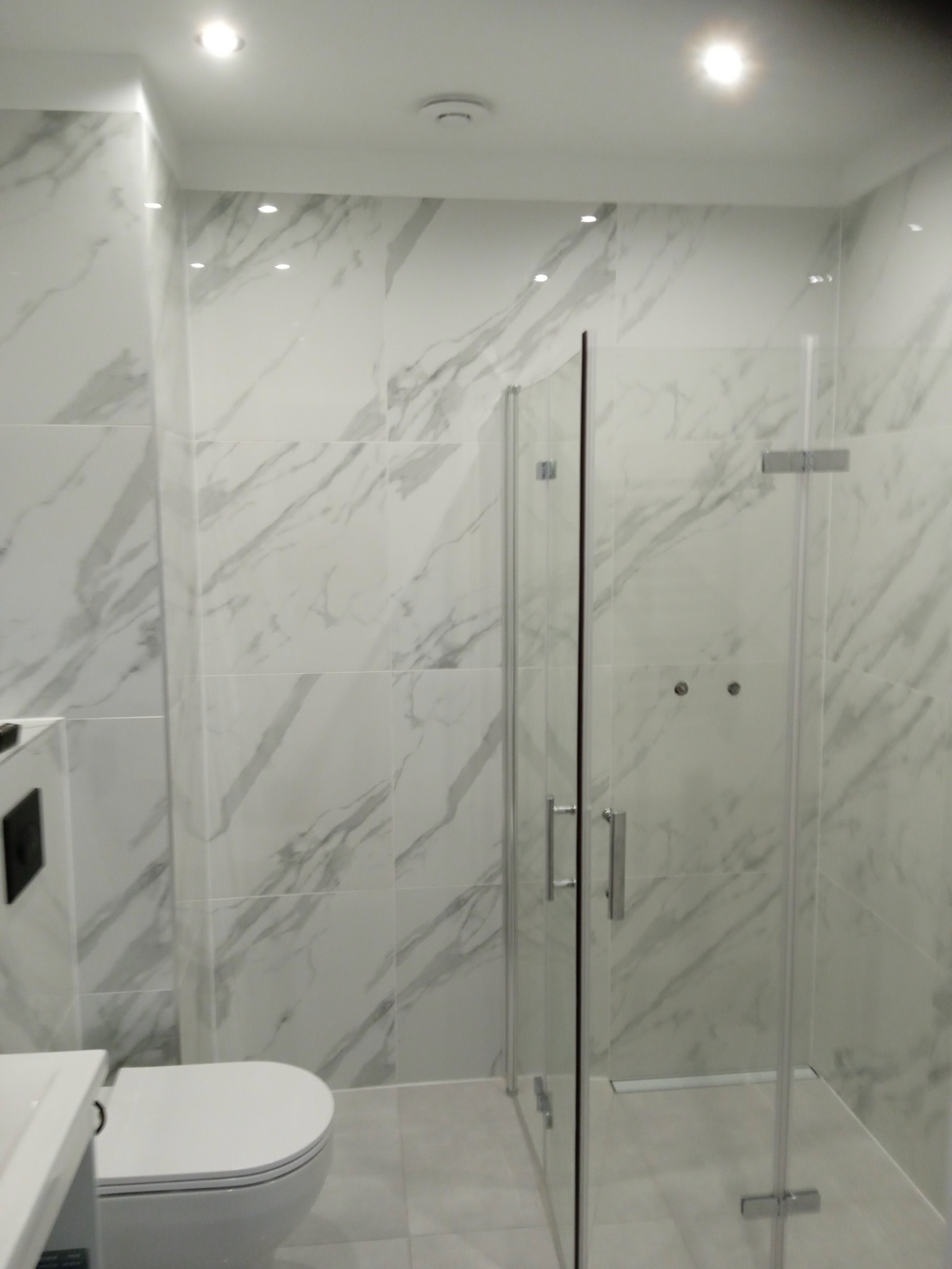 Wykończona łazienka w Gdańsku z kabiną prysznicową i toaletą w stylu marmuru carrara, z widocznymi chromowanymi uchwytami i minimalistycznym designem.