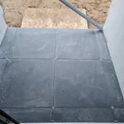 Ułożone, ciemnoszare płytki podłogowe z krzyżykami dystansowymi, widoczne elementy konstrukcyjne i niezagospodarowane podłoże.