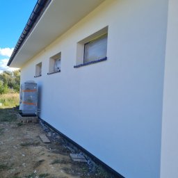 FIRMA FENSTER UND BAU Ewa Siegler - Świeżo pomalowana, biała elewacja budynku z zabezpieczonymi oknami folią malarską, widoczny klimatyzator owinięty folią ochronną.