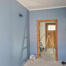 FIRMA FENSTER UND BAU Ewa Siegler - Świeżo pomalowane na niebiesko ściany w mieszkaniu w Dobrej, z widoczną drewnianą futryną drzwi, drabiną i wiadrem z farbą w rogu.