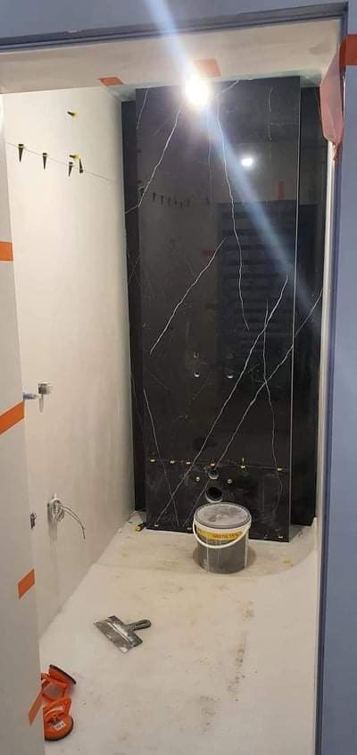 Montaż czarnych płytek imitujących marmur w łazience, widoczny kubeł z zaprawą, szpachelka i przyssawki do płytek.