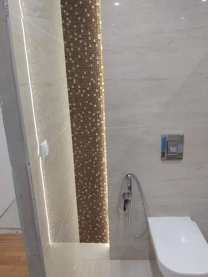 Wykończona łazienka w Pakości z beżowymi płytkami imitującymi marmur, mozaiką z brązowych kwadratów, podświetleniem LED i wiszącą toaletą z bidetką.