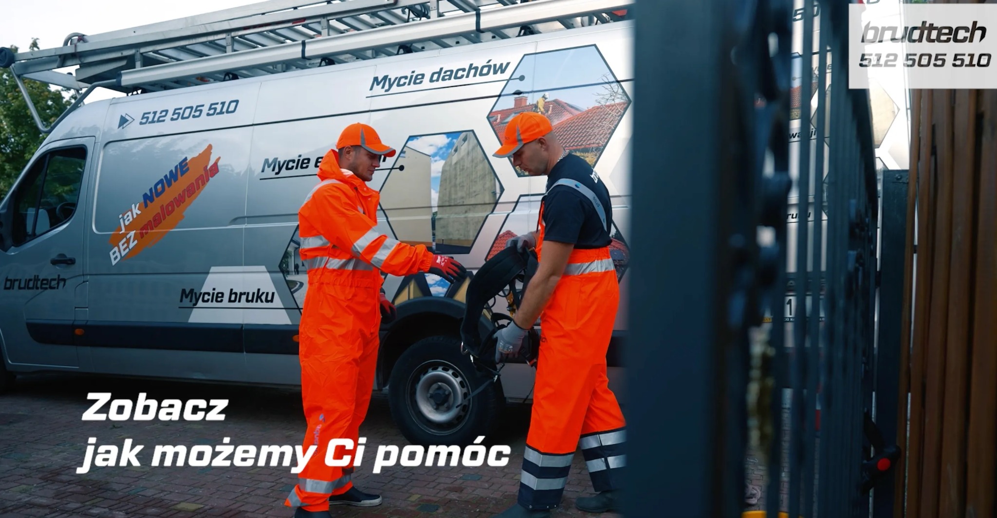 Dwóch pracowników w pomarańczowych kombinezonach przy samochodzie firmowym z napisem 'Mycie dachów' i 'Mycie bruku', przygotowujących sprzęt do pracy.