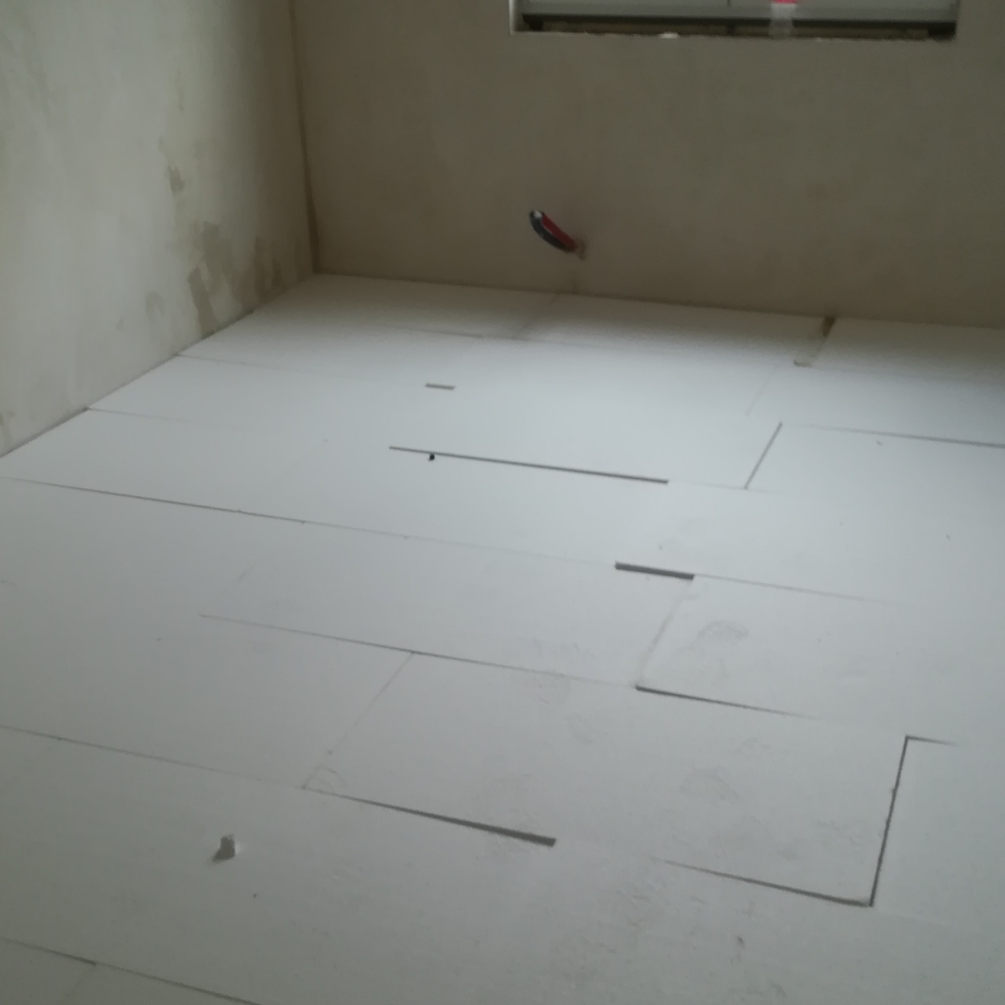 Białe płyty izolacyjne ułożone na podłodze w surowym wnętrzu, przygotowane pod wylewkę.