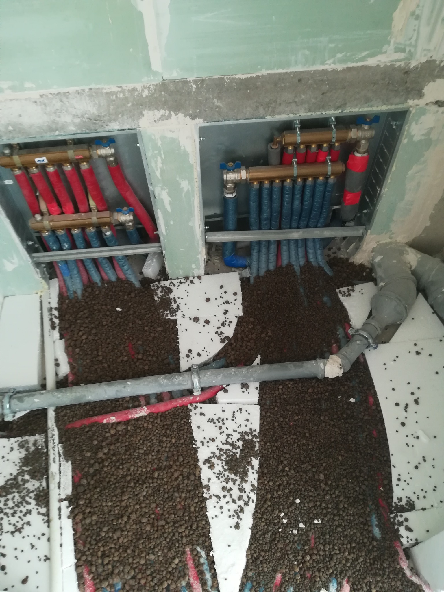 Rozdzielacz ogrzewania podłogowego, rury grzewcze w izolacji, styropian i keramzyt rozsypany na podłodze w trakcie montażu instalacji.