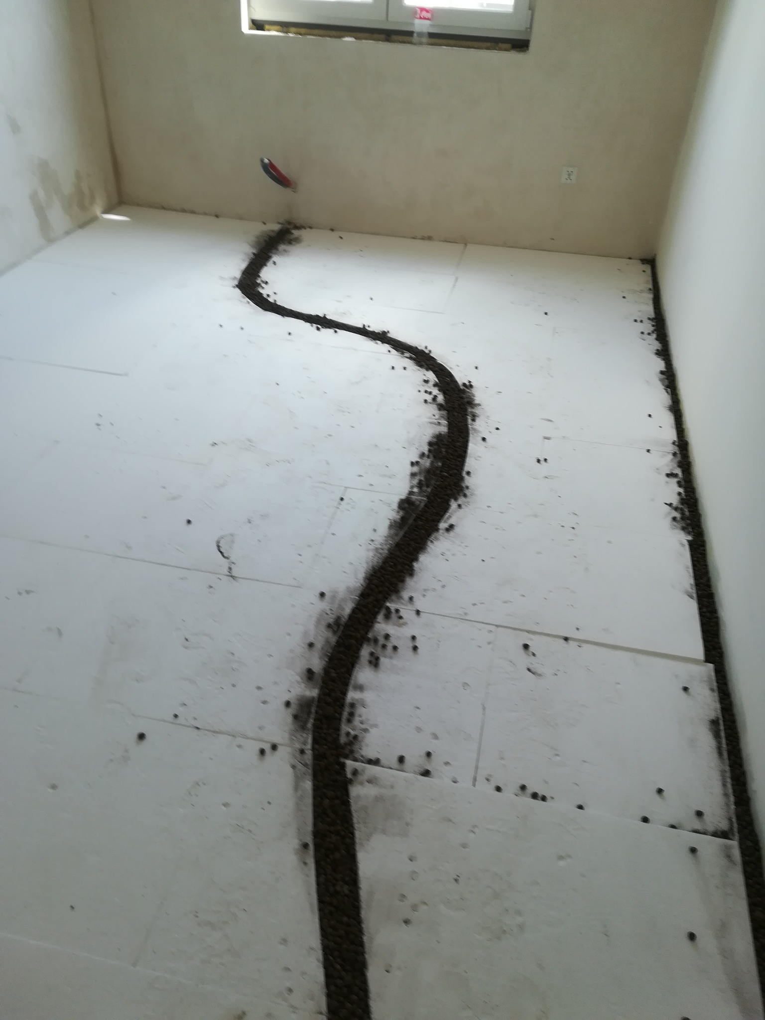 Przygotowanie podłoża pod posadzkę: rozłożony styropian z widocznymi liniami podsypki wyrównującej w kształcie węża, przy ścianach również podsypka.