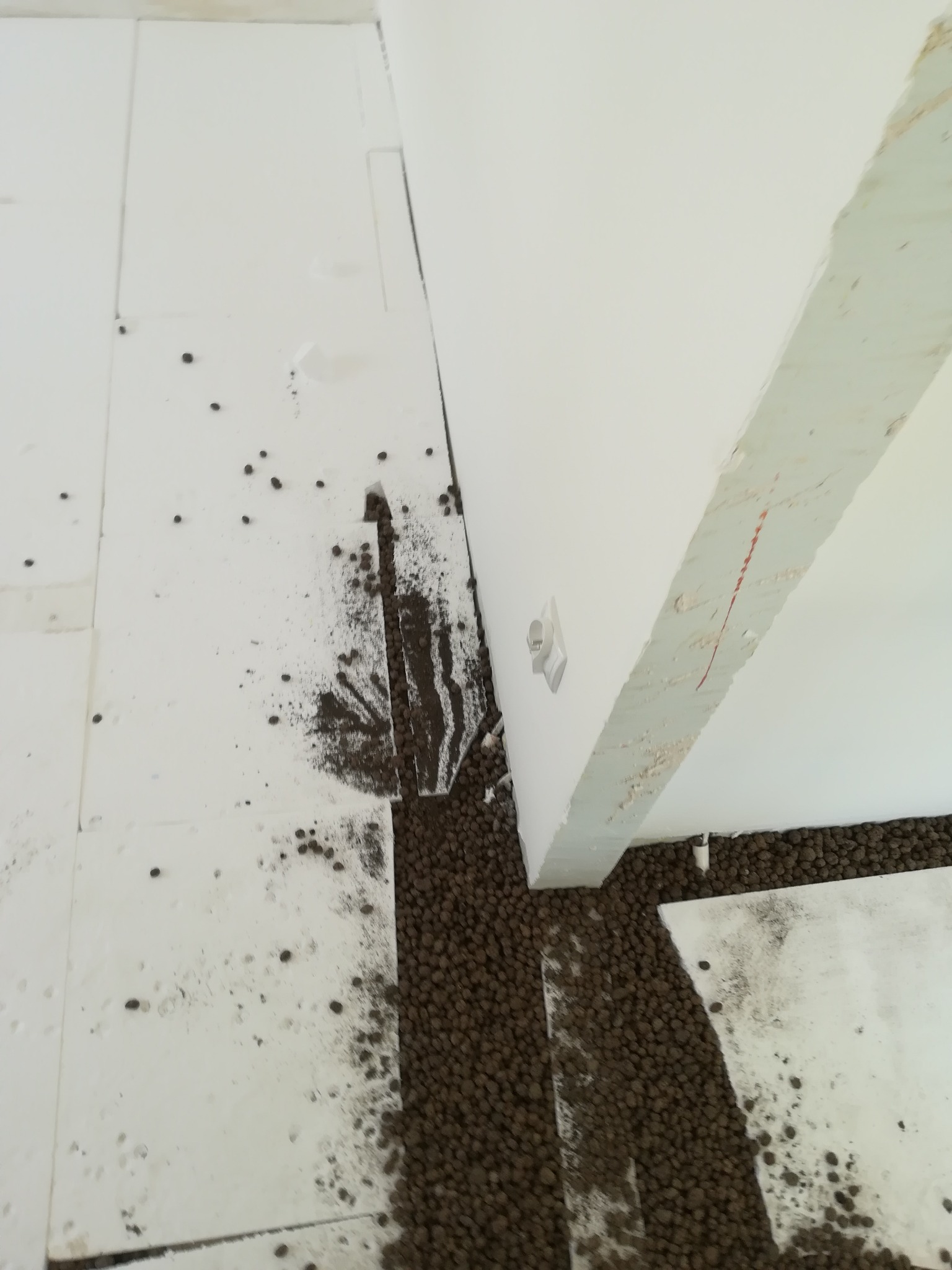 Przygotowanie podłoża pod wylewkę w Bytomiu: białe płyty styropianowe rozłożone na podłodze, częściowo zasypane brązowym granulatem izolacyjnym, widoczna ściana z instalacją elektryczną.