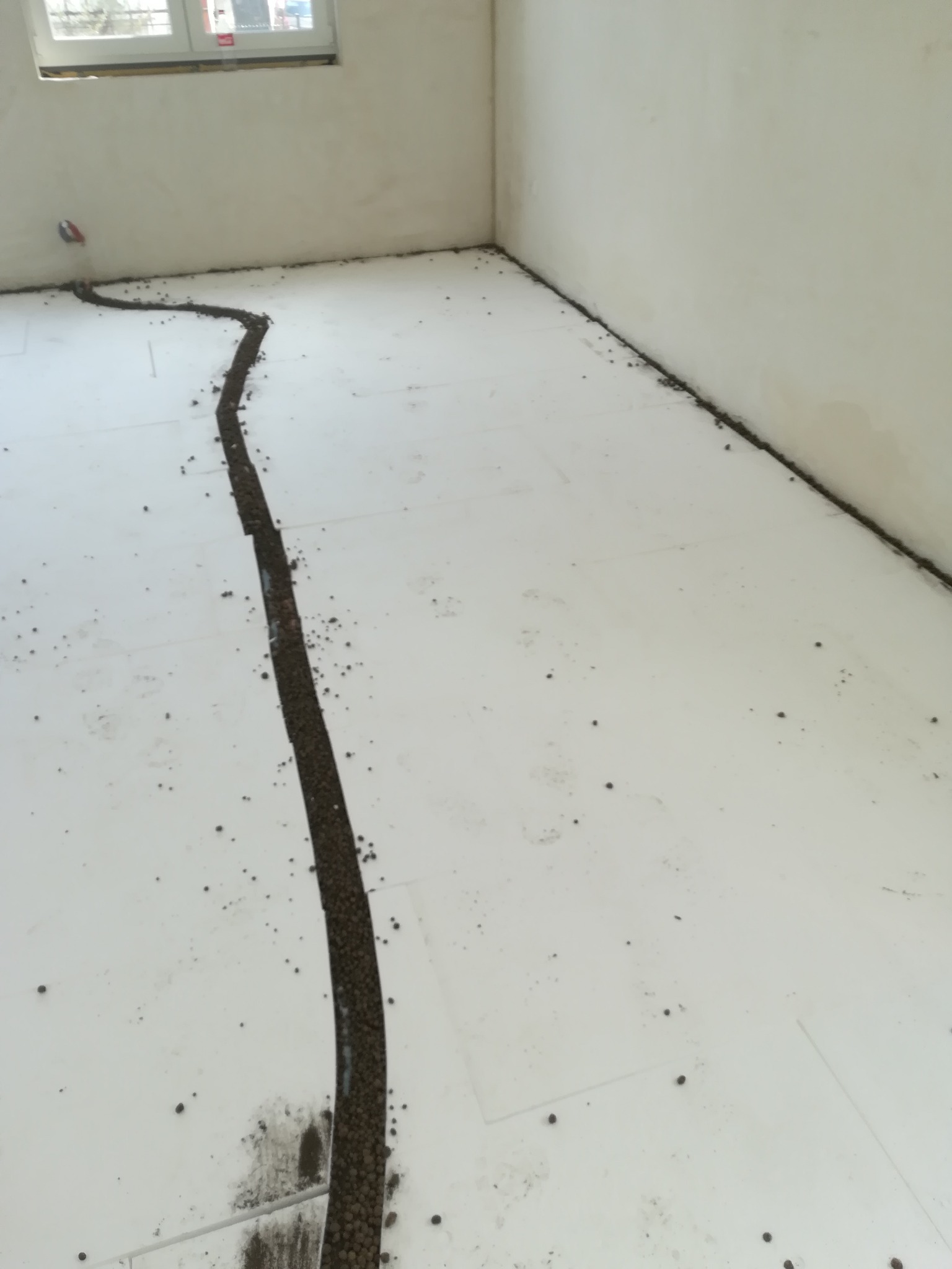 Przygotowanie podłoża pod wylewkę: styropianowe płyty z wyciętym rowkiem wypełnionym granulatem izolacyjnym w jasnym pomieszczeniu z oknem.