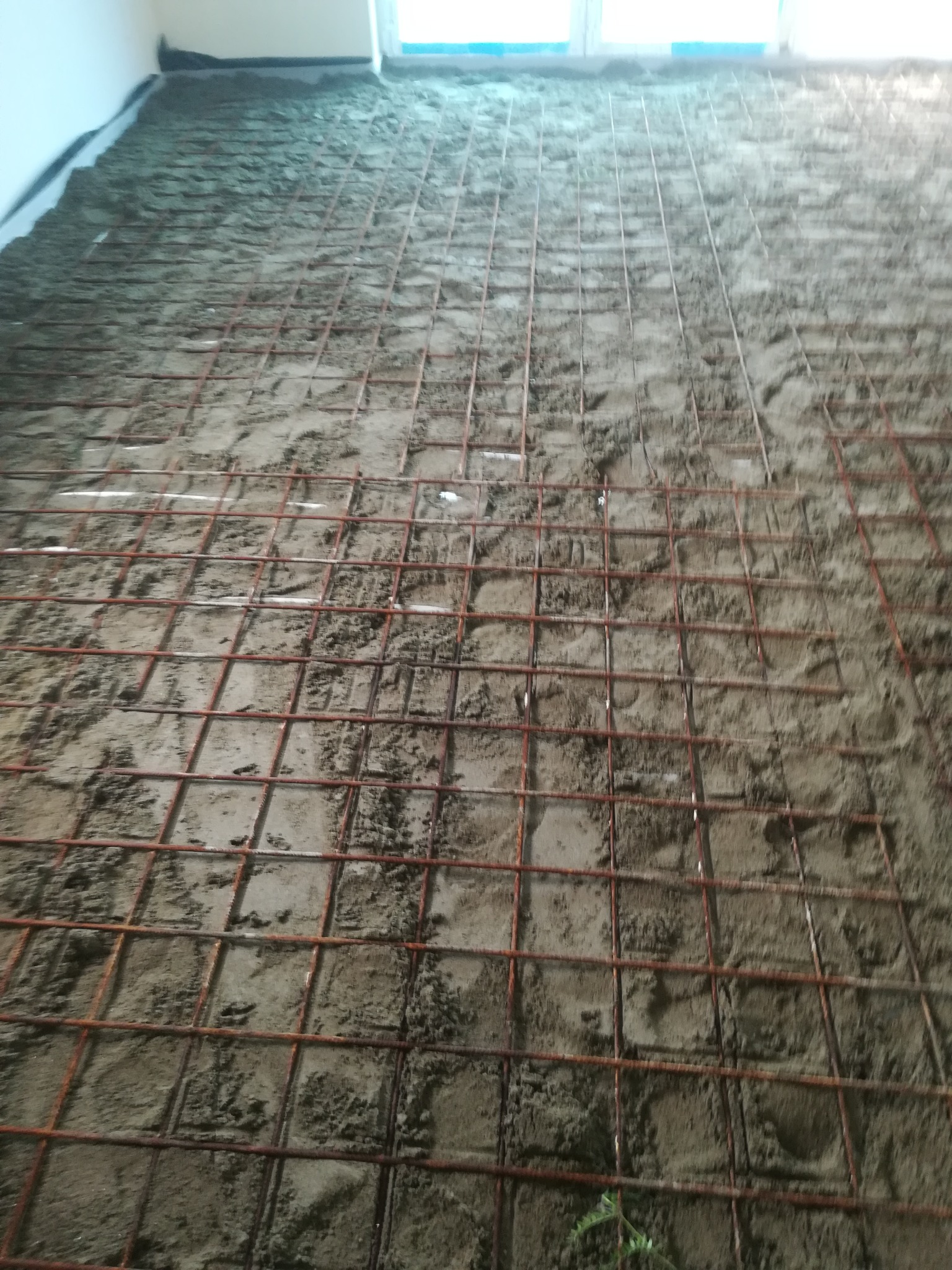 Przygotowanie podłoża pod wylewkę z siatką zbrojeniową na nierównej powierzchni, widoczne folie przy ścianach.