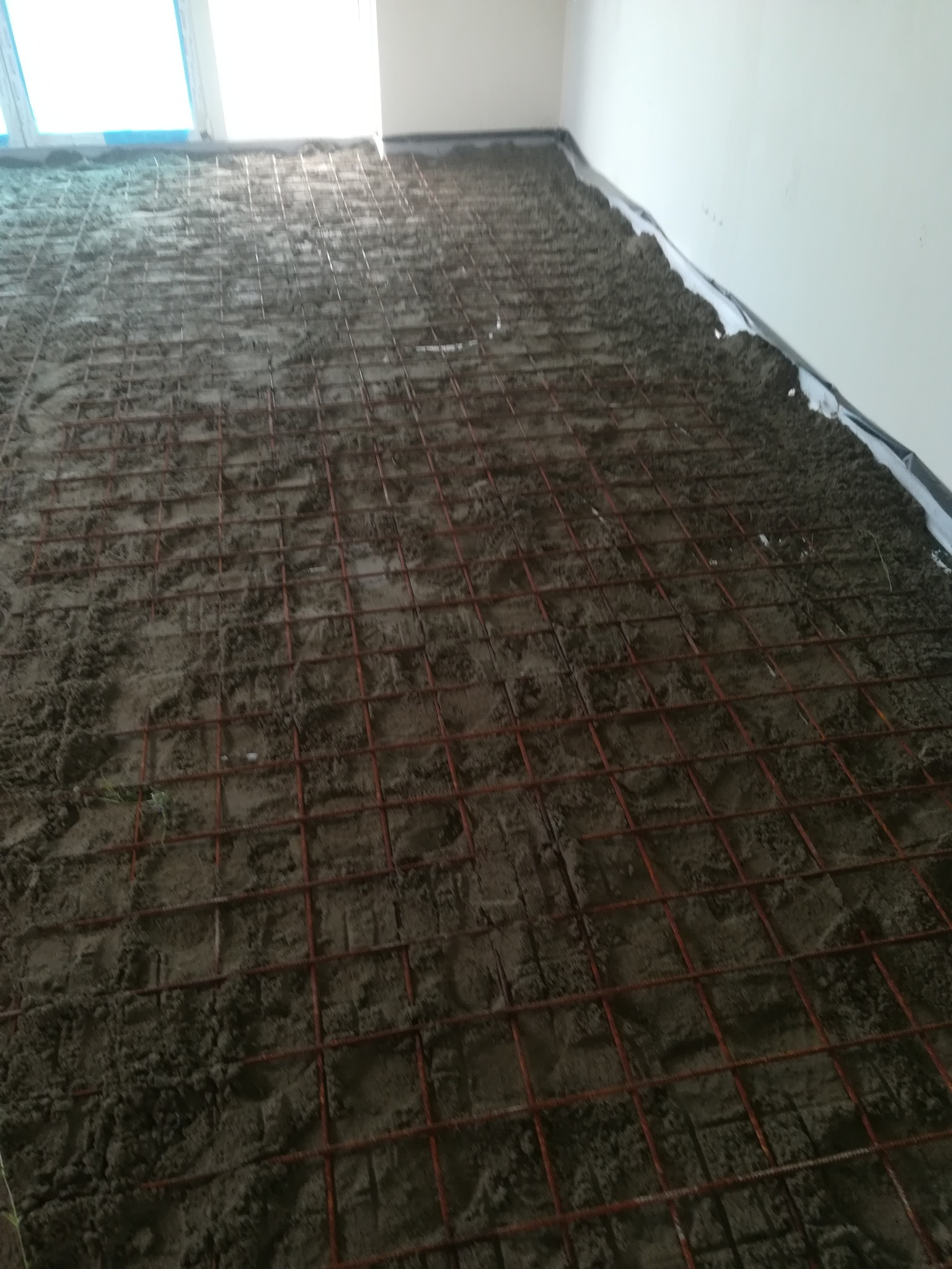 Przygotowanie podłoża pod wylewkę: siatka zbrojeniowa na warstwie izolacji, widok z góry na nierównomiernie rozłożoną zaprawę.