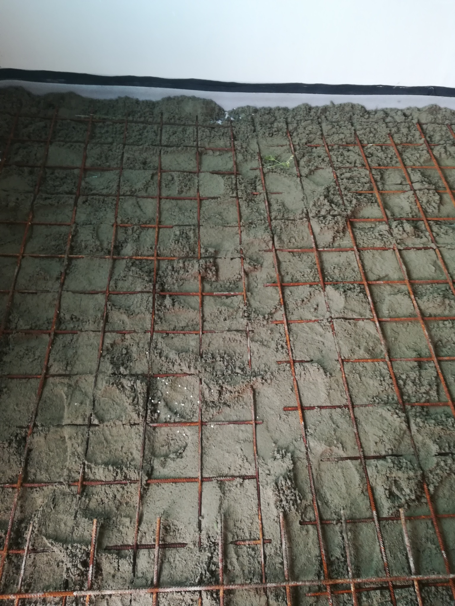 Świeżo wylana, szara masa betonowa z widoczną siatką zbrojeniową na podłożu, przygotowana pod wylewkę.